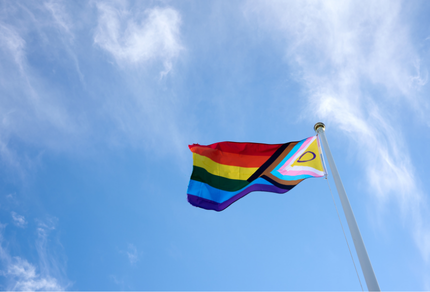 Progress pride flag waving in the wind against a blue sky