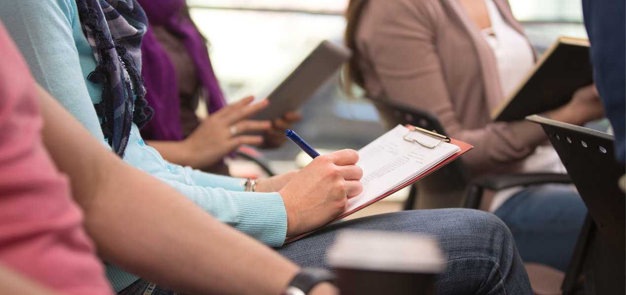 Close up of a student's hands taking notes on a clipboard.