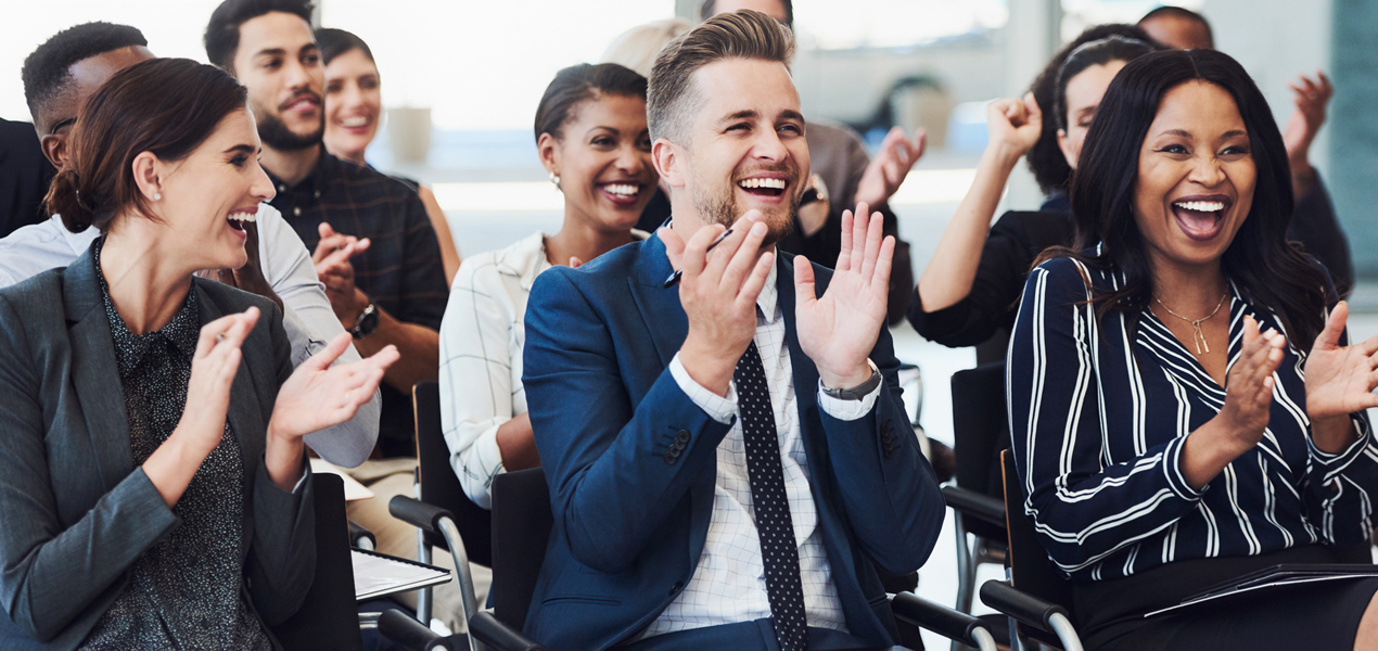 An audience in business attire clapping and cheering during a conference.